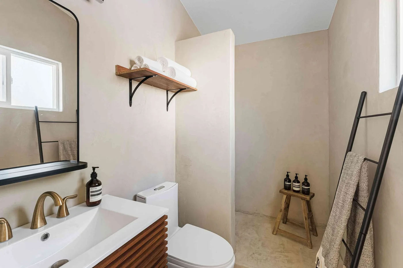 Remodeled bathroom with a floating wood vanity, brass faucet, and plaster-look walls