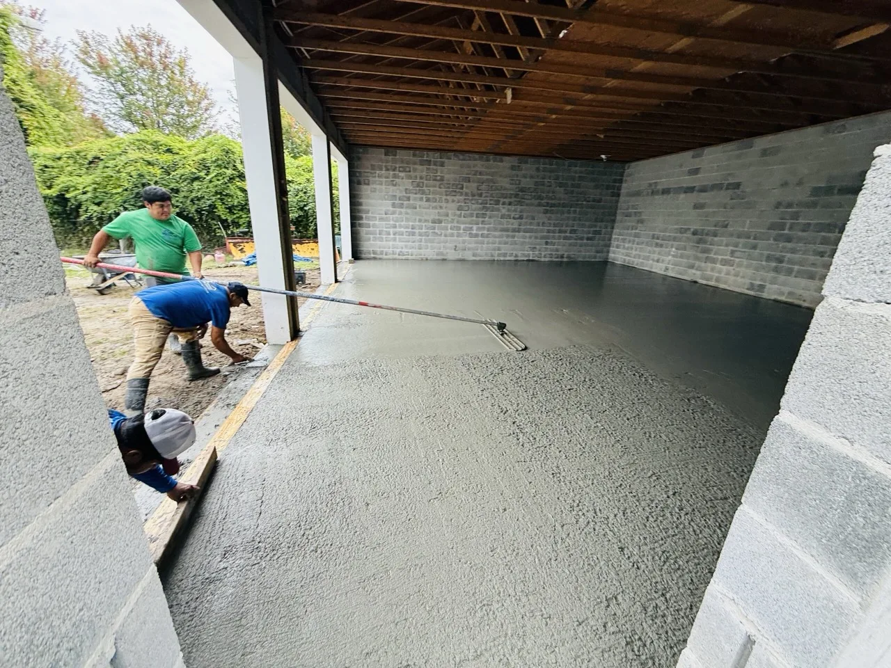 A concrete crew screeding and finishing a freshly poured slab at a home