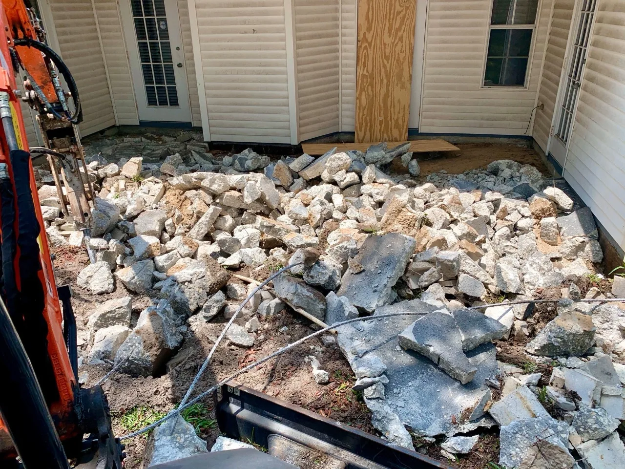 A small excavator removing broken-up old concrete during a slab tear-out at a home