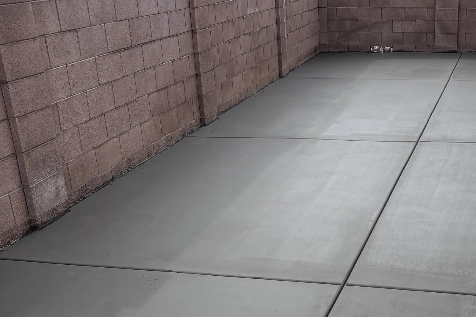 Freshly finished concrete slab with saw-cut control joints between block walls